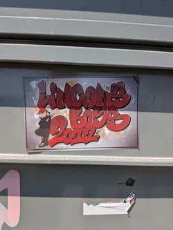 Street sticker A rectangular sticker featuring red bubble-letter graffiti text 'LINCON'S BOYS 2012' on a textured grey background. A cartoon character wearing a red cap and black hoodie stands on the left side.