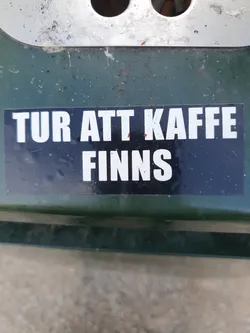 A black sticker with white text on a dark green surface. The text says "TUR ATT KAFFE FINNS" which translates from Swedish to English as "Time for coffee exists".