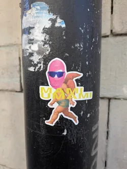 Street sticker The sticker features a stylized, winged figure resembling a classical cherub or putto, depicted with plump, light-skinned limbs and small, reddish-brown wings. Its lower body is covered by a teal-green loincloth. The head of the figure is replaced by a vibrant pink balaclava or ski mask, under which a pair of sleek, blue-tinted futuristic sunglasses are worn. The figure is in a dynamic pose, appearing to run or stride forward. Bold, yellow capital letters spelling 'MAXIMI' with a white outline are placed horizontally across the figure's midsection, partially obscuring its body. The entire design is cut out with a clean white border.