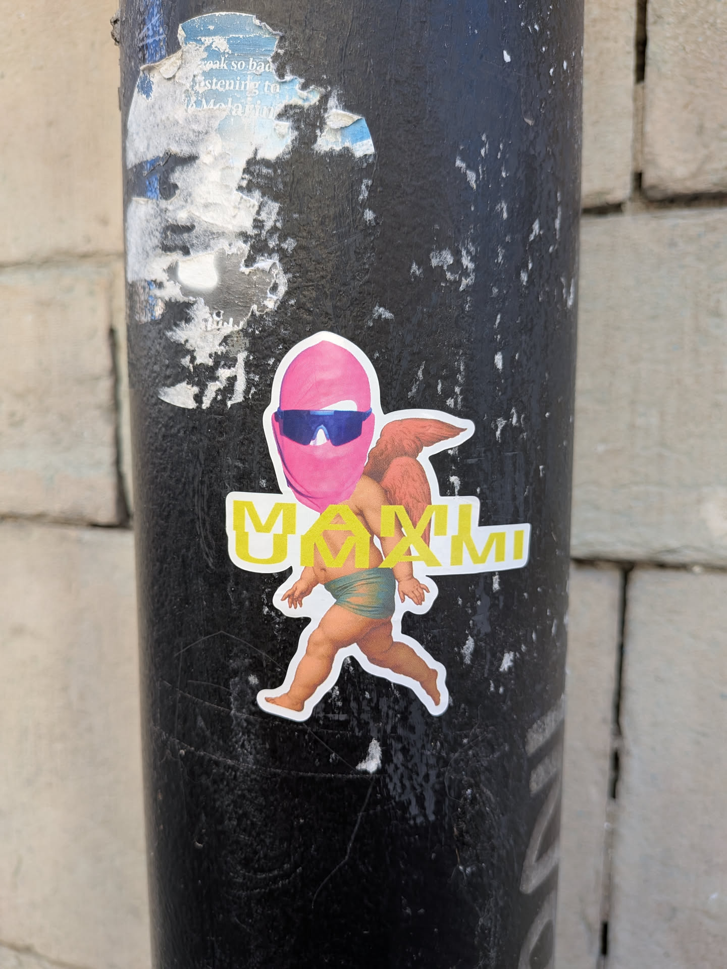 The sticker features a stylized, winged figure resembling a classical cherub or putto, depicted with plump, light-skinned limbs and small, reddish-brown wings. Its lower body is covered by a teal-green loincloth. The head of the figure is replaced by a vibrant pink balaclava or ski mask, under which a pair of sleek, blue-tinted futuristic sunglasses are worn. The figure is in a dynamic pose, appearing to run or stride forward. Bold, yellow capital letters spelling 'MAXIMI' with a white outline are placed horizontally across the figure's midsection, partially obscuring its body. The entire design is cut out with a clean white border.