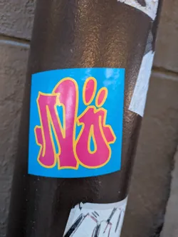 Street sticker The sticker is predominantly a bright, sky blue. Centered on this blue background are stylized, bubble-like letters rendered in a vibrant pink outline with a yellow inner border. The letters appear to form a word or tag, with a distinct shape resembling an 'N' or a stylized monogram, followed by two small, oval shapes that could be dots or part of the lettering. The edges of the sticker are clean and appear to be slightly rounded.