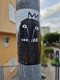 Street sticker A black and white drawing of a monster with a crown. It looks like a simple, hand-drawn illustration with visible texture on the sticker.