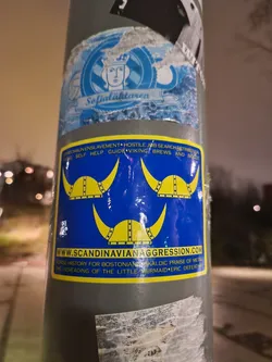 A sticker featuring three Viking helmets and the website address www.scandinavianaggression.com. The text on the sticker also mentions Norse history for Bostonians, Skaldic praise of metal, and the beheading of the Little Mermaid.