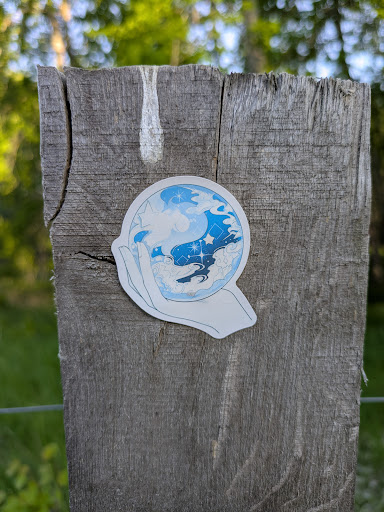 This aesthetic sticker features a hand holding a crystal ball. Inside the crystal ball, there are celestial elements such as clouds, stars and waves, creating a dreamlike and mystical atmosphere. The color palette is in light blue tones, which enhances the overall aesthetic appeal.