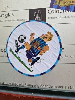 Street sticker A round sticker featuring a cartoon illustration of a man playing soccer. He has light skin, blond hair, and is wearing a blue and white soccer uniform. He is kicking a soccer ball with a determined expression on his face. The background of the sticker is white with a touch of green grass.  The sticker has a dark blue border.