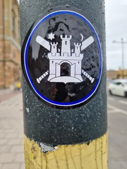 Street sticker This round sticker displays a black and white illustration of a castle with crenelations, a gate, and two towers.  The castle is centrally positioned, with a baseball bat crossing over another on each side.  Above the castle, there's a six-pointed star to the left and a crescent moon to the right. The sticker has a black background with a blue outer ring.