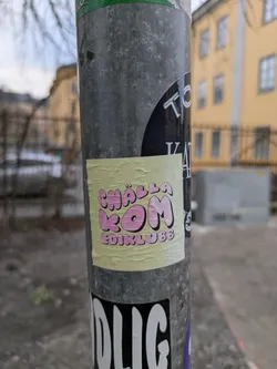 A yellow sticker with pink text. The text says "CHÄLLA KOM EDIKLUB88".  It's stuck on a grey pole with other stickers.