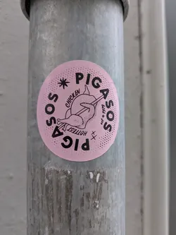Street sticker This is a round, pink sticker with black typography and an illustration, affixed to a grey metal pole. The central graphic depicts a stylized chicken or rooster with an arrow piercing through it. The text "PIG" is prominently displayed at the top and inverted at the bottom of the circle. Along the left edge, the word "SOS" is written curving upwards, and along the right edge, "ASOS" curves downwards, accompanied by "est * 1979". Smaller text near the chicken reads "CHICKEN" and "HOTTEST". The pink background has a subtle dotted texture, particularly around the edges.