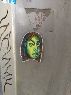 Street sticker A sticker of a stylized female face with green and yellow tones. The style is reminiscent of a sketch or drawing, with visible lines and shading.