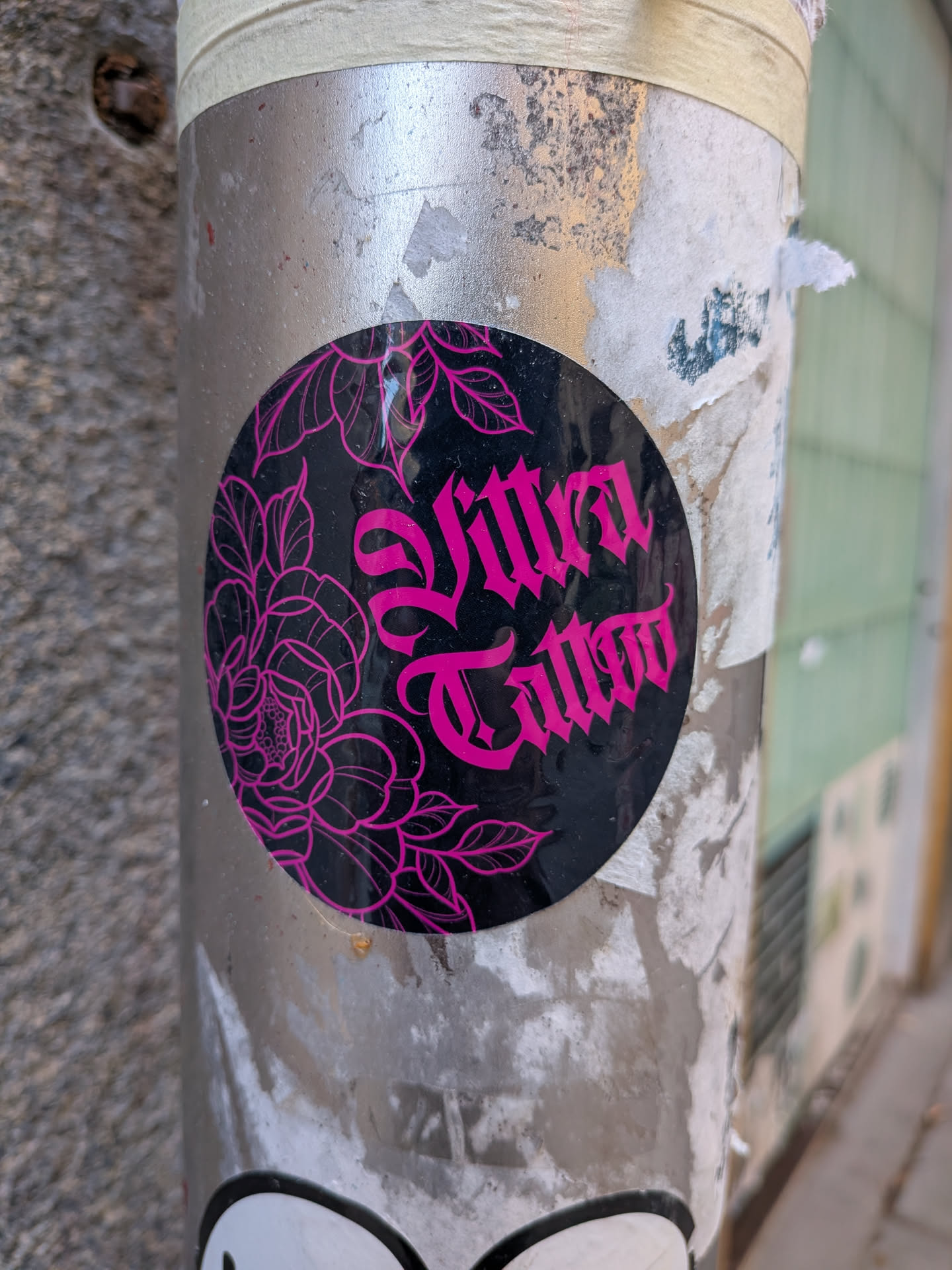A round black sticker featuring pink line-art flowers on the left and the text 'Vitra Tattoo' in a gothic font on the right.