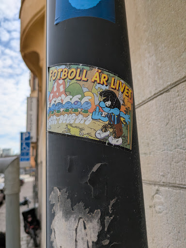 The sticker shows a group of Smurfs and a Smurfette, with the text "Fotboll är livet" above them. The Smurfette is wearing a football jersey and has her middle finger up.