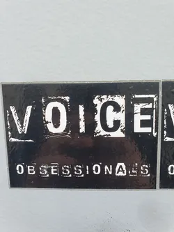 Street sticker Black and white sticker with the text "VOICE" in a bold, blocky font, and below it, "OBSESSIONALS" in a similar style. The sticker has a slightly distressed or grunge aesthetic.
