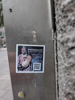 Street sticker Square sticker featuring a photo of a woman holding a thin child on the left. The right side contains Swedish text urging a boycott of Israel, the website 'Raddagaza.nu', and a QR code.