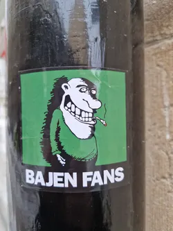 Street sticker A green sticker with a cartoon drawing of a man smoking a cigarette. The text 'BAJEN FANS' is written at the bottom of the sticker.