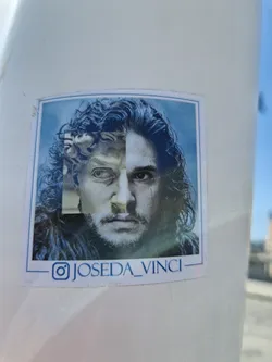 Street sticker This sticker features a striking image that blends Kit Harington's portrayal of Jon Snow from Game of Thrones with a classical Renaissance statue. The image is expertly collaged to create a seamless visual juxtaposition, playing with ideas of time and artistic influence.  The artist's Instagram handle is visible at the bottom.
