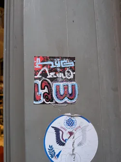 A rectangular sticker with a black background, featuring intricate graffiti-style lettering. The upper portion displays stylized text in light blue and white, with red paint splatters, appearing to spell 'TRUE'. The lower portion showcases larger, bubble-style letters in red, blue, and purple with white outlines, forming the word 'LAW'. The overall design is energetic and colorful, with visible texture and slight wear on the sticker's edges, indicating it's a physical sticker adhered to a surface.