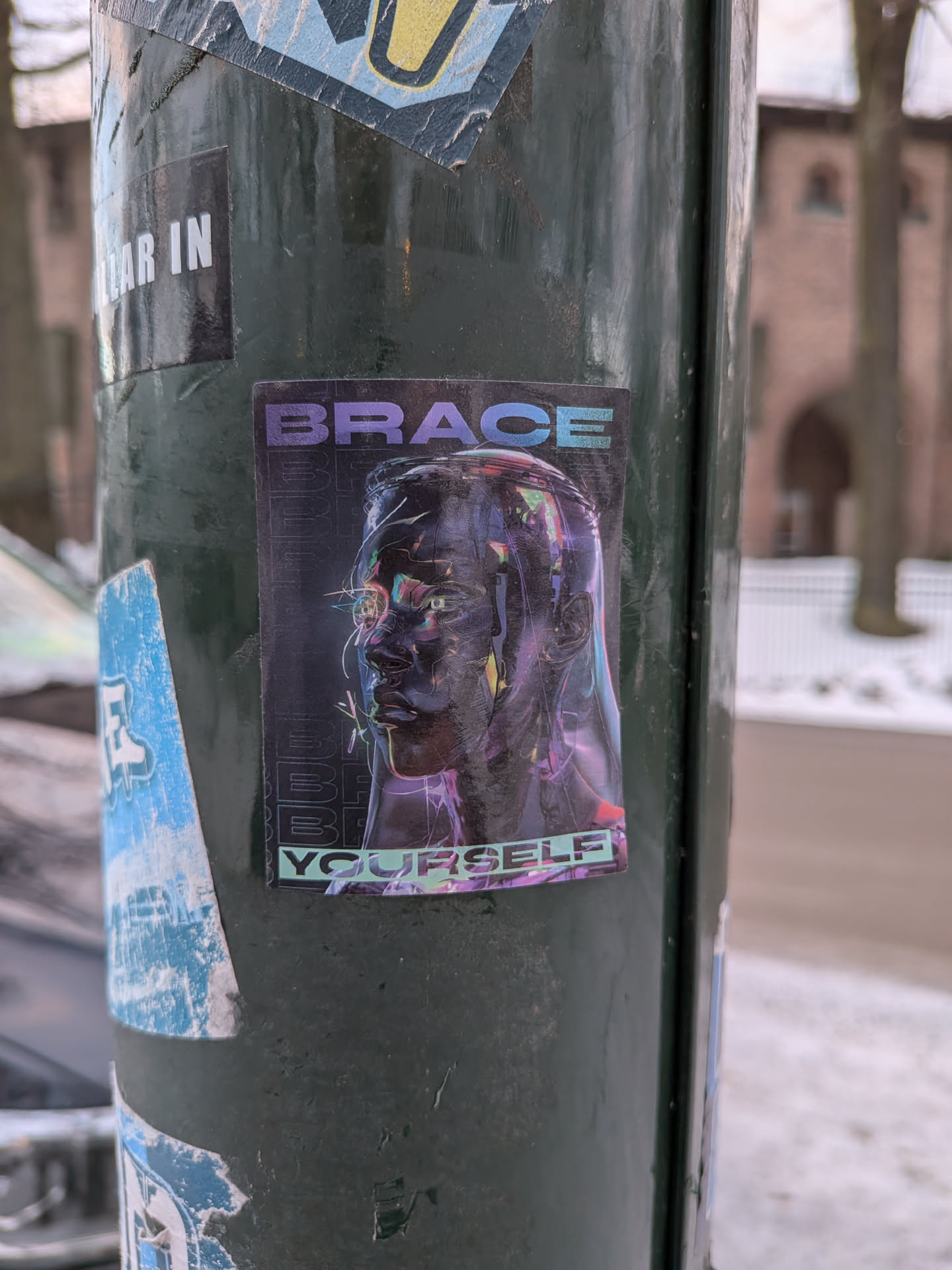 Street sticker The sticker showcases a stylized, dark-toned human head in profile, facing left, rendered with a metallic or glossy finish. The eyes glow with an intense green light, and the head is surrounded by sharp, luminous lines in shades of purple, blue, and pink, giving it a futuristic, digital, or holographic appearance. The background is dark, almost black, with faint, repeated vertical text. The word 'BRACE' is prominently displayed in purple block letters at the top, and 'YOURSELF' in teal block letters at the bottom, completing the phrase 'BRACE YOURSELF'. The overall aesthetic is reminiscent of cyberpunk or sci-fi themes, with elements of glitch art and neon lighting.