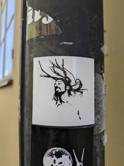 The sticker features a black and white illustration of a person's face in profile. The hair is styled to resemble tree branches or antlers, adding an intriguing and artistic element to the design.