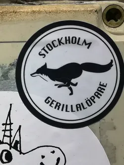 Street sticker A circular sticker featuring a minimalist black and white design. It has a thick black outer ring enclosing a white background. Centered within the circle is a stylized black silhouette of a fox in a dynamic running or leaping pose, facing left with its tail extended. Curved along the top inner edge of the circle is the word 'STOCKHOLM' in black uppercase letters, and along the bottom inner edge is 'GERILLALÖPARE', also in black uppercase letters.