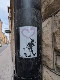 Street sticker A rectangular white sticker depicting a black silhouette of Pippi Longstocking holding a paintbrush. Above her is a dripping pink heart. A paint can sits at her feet, and the text 'IRON' is printed in the bottom-left corner.