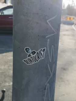 Street sticker The sticker features a stylized, monochromatic illustration of a person, likely male, from the chest up. The figure wears a dark fedora-style hat, dark sunglasses, a dark suit jacket, and a dark bow tie. The face is depicted with minimal features, primarily the sunglasses and a defined jawline, in a lighter blue-grey tone. The entire illustration is outlined in white, giving it a distinct cut-out appearance. Below the figure, the word "RUNTourist" is written in a bold, somewhat distressed or wavy sans-serif font, also in dark grey/black with a white outline. The overall aesthetic is clean yet edgy, with a limited color palette of black, white, and a muted blue-grey.