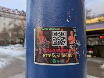 Street sticker A sticker advertising a new album by the band ZAGWERK.  The sticker features a QR code, a website address, and the Spotify logo.  The design is dark with two figures in red/orange.