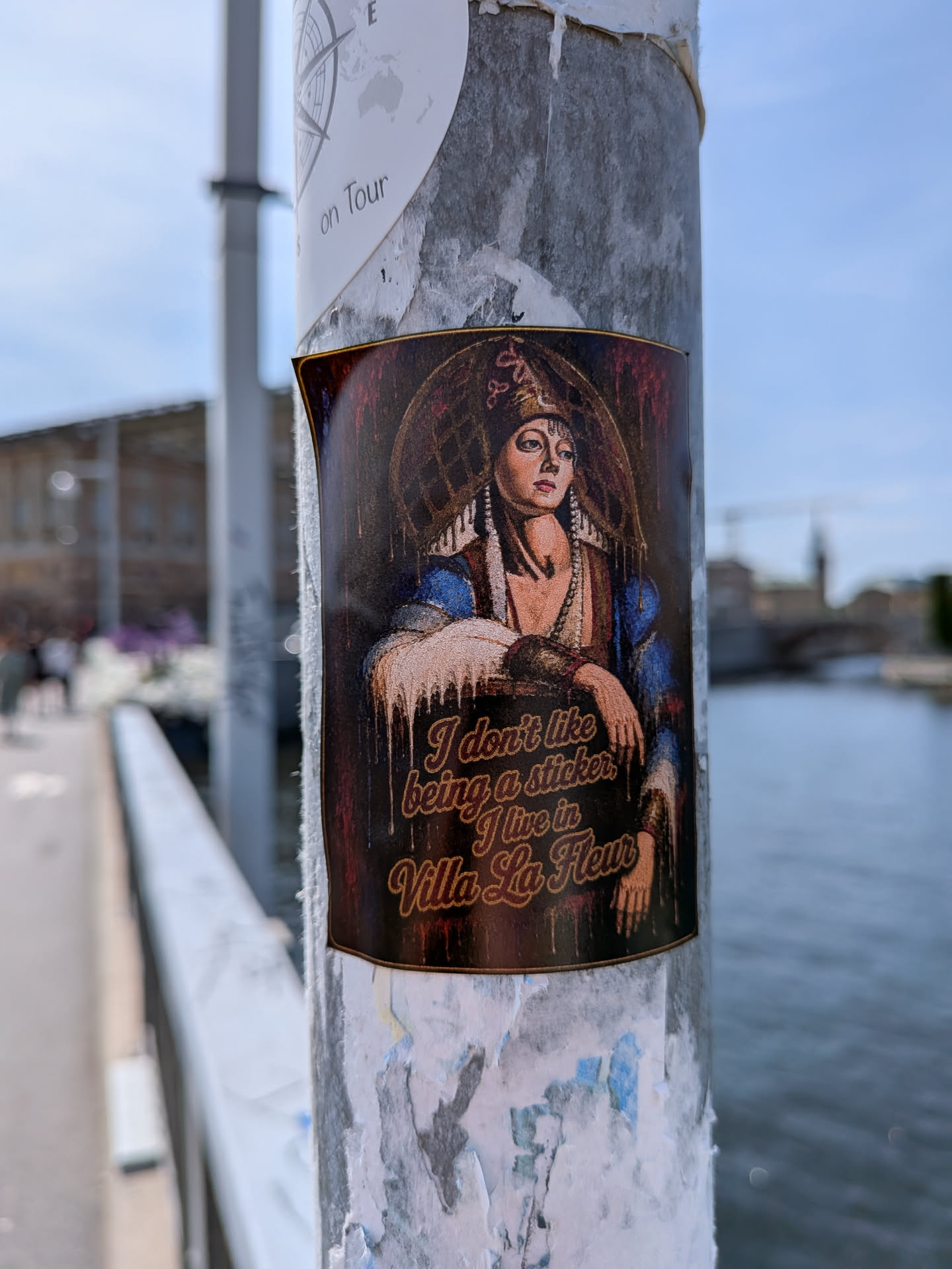 A rectangular sticker depicting a classical portrait of a woman in traditional, ornate clothing and headwear. The background is dark and textured. Gold, cursive text at the bottom reads, 'I don't like being a sticker, I live in Villa La Fleur'.