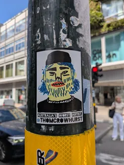 Street sticker A rectangular sticker featuring a hand-drawn portrait of a man with a yellow face, blue hair, a blue-lined beard, and a black beanie. The text below reads 'AUSTRALIA'S WORST ARTIST.' and '@THOMCROWHURST'.