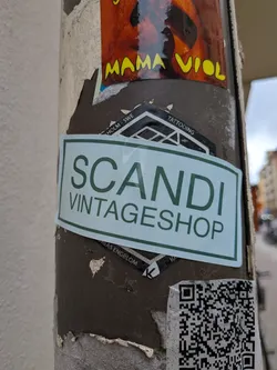 A rectangular sticker with a light mint green background and a dark green border. The text 'SCANDI' is written in a large, clean, sans-serif font, with 'VINTAGESHOP' written in a smaller font directly underneath. The sticker is affixed to a metal post, partially covering another sticker.