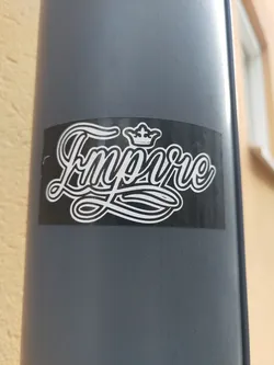 Street sticker A black and white sticker with the word "Empire" stylized in a script font with a crown above it.  The sticker is affixed to a gray pole.