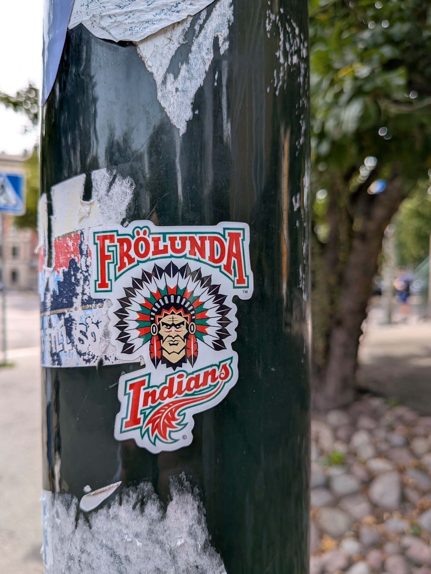 Die-cut sticker of the Frölunda Indians logo on a dark pole. Features a Native American chief in a feathered headdress, with 'FRÖLUNDA' arched above and 'Indians' below in red and green.