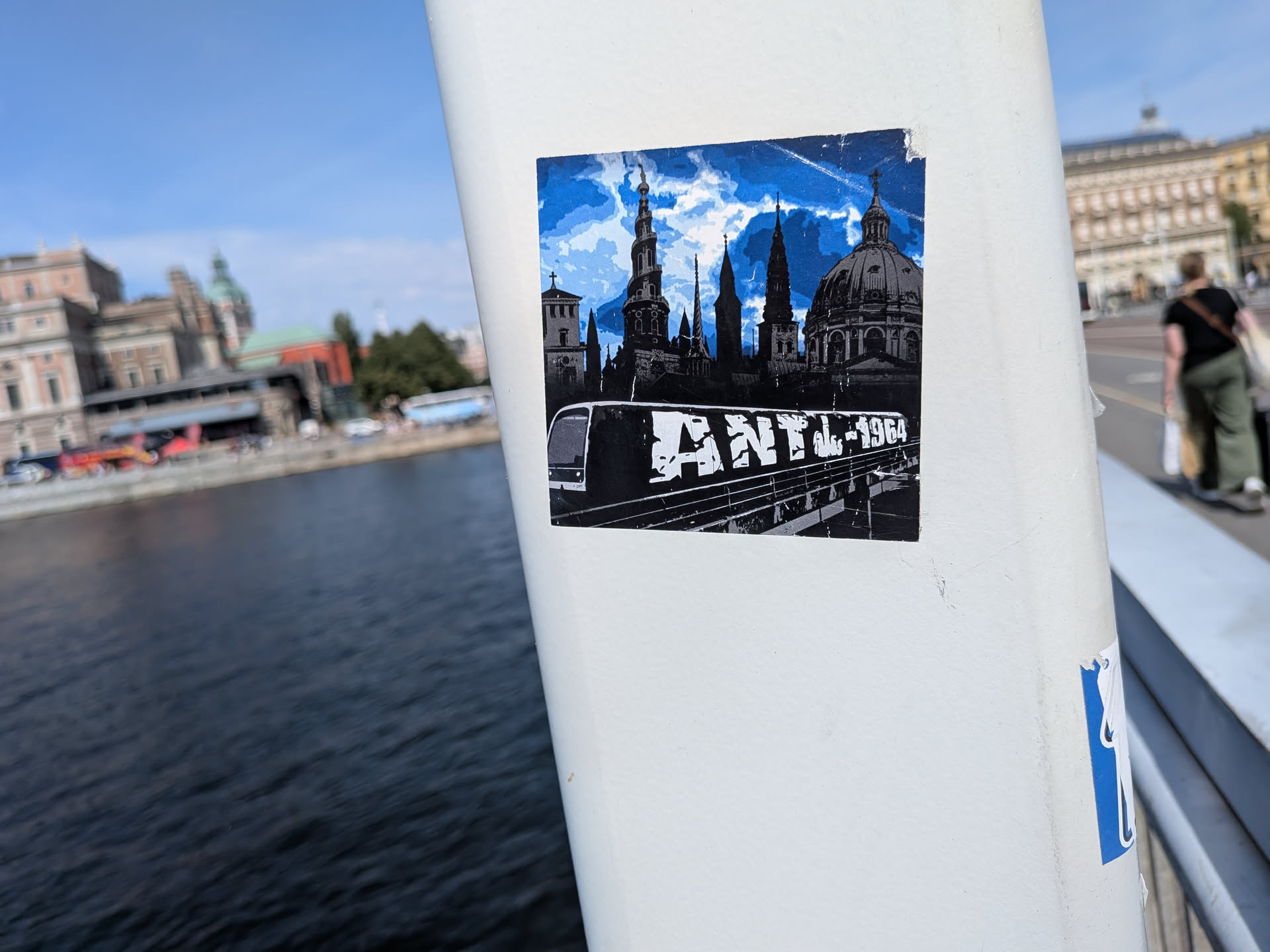 A square sticker featuring a black-and-white silhouette of Copenhagen's historic spires and domes against a blue sky. The foreground shows a train car painted with white 'ANTI-1984' graffiti.