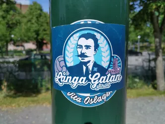 Street sticker A sticker featuring a stylized portrait of a man with a mustache, laurel wreaths, and a depiction of a building, possibly a castle or town hall.  The text "Långa Gatan Stockholm" is prominently displayed in a stylized script font.  The bottom of the sticker features the word "Viva Oslagar".
