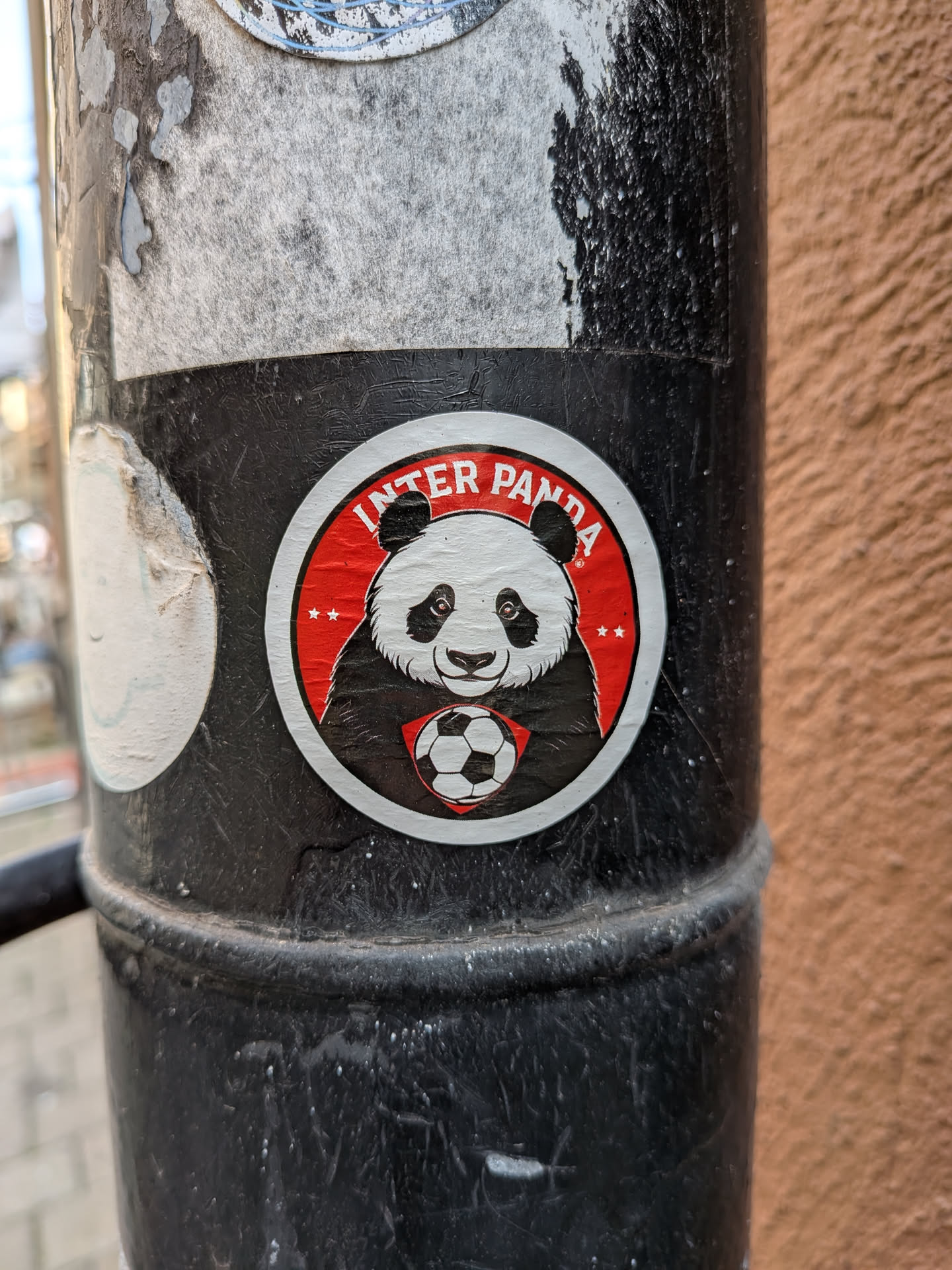 A round sticker depicting a panda mascot holding a soccer ball. The design uses a red and black color scheme with white accents, featuring the arched text 'INTER PANDA' and small stars.