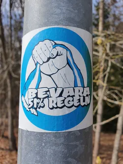 Street sticker The sticker features a stylized fist clutching a ribbon, set against a blue circular background. The text "BEVARA 51% REGLN" is prominently displayed beneath the fist.  The image suggests a message of preserving or maintaining something, possibly related to a rule or regulation (51% possibly referring to a majority).