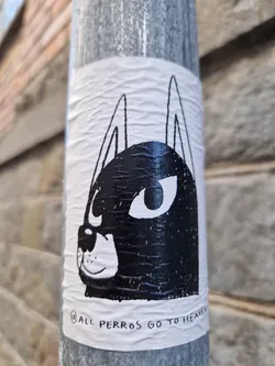 A black and white sticker of a dog's face with big eyes. The text at the bottom says "All perros go to heaven".