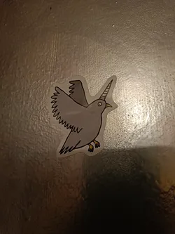 A sticker of a gray pigeon with a single, spiraled unicorn horn on its head. The pigeon is depicted in flight, its wings spread. The art style is simple, with black outlines and minimal detail. It's a whimsical and slightly surreal image.