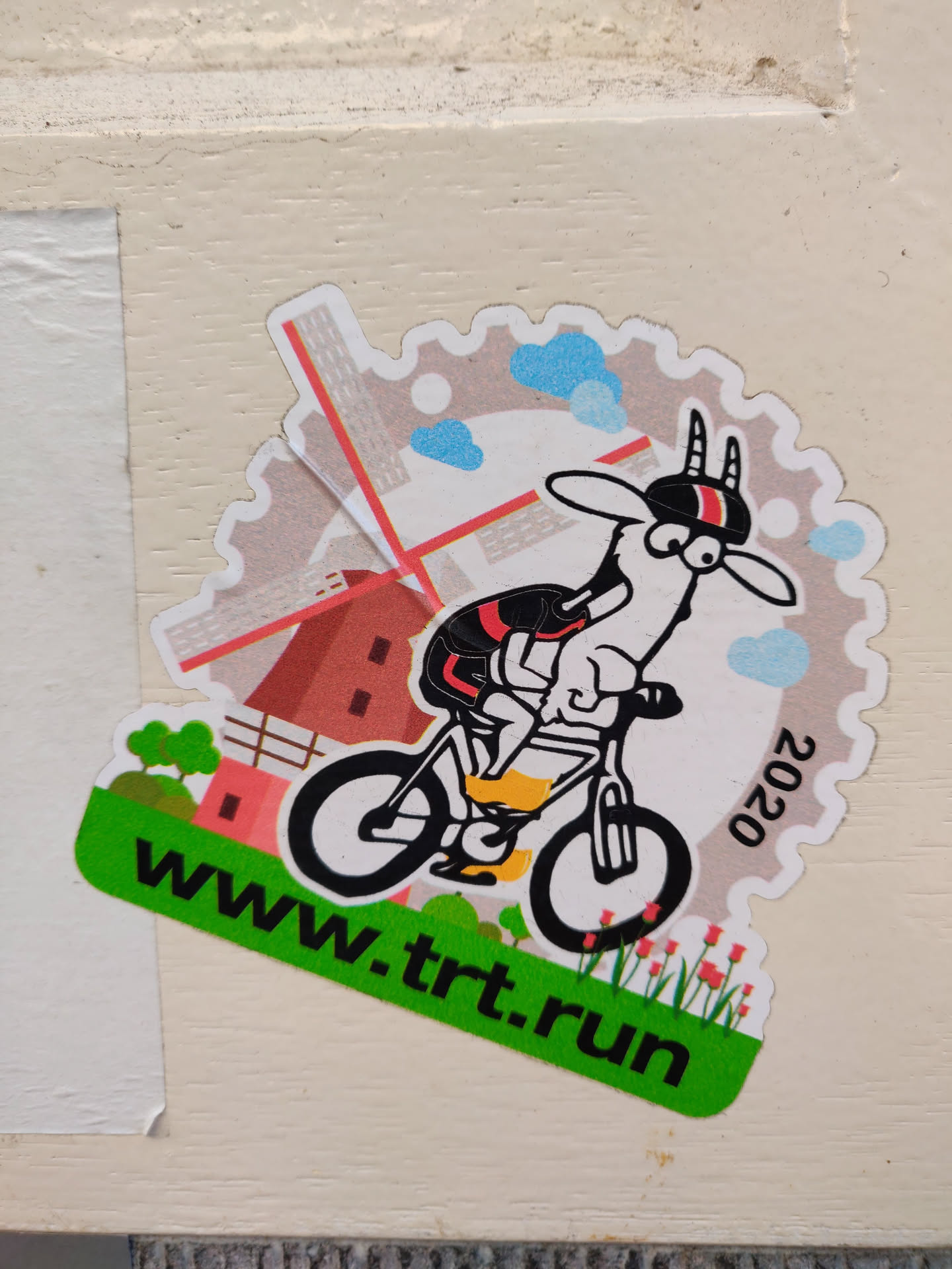 A sticker featuring a cartoon goat riding a bicycle in front of a windmill. The year 2020 is visible on the sticker.  The website www.trt.run is printed at the bottom.