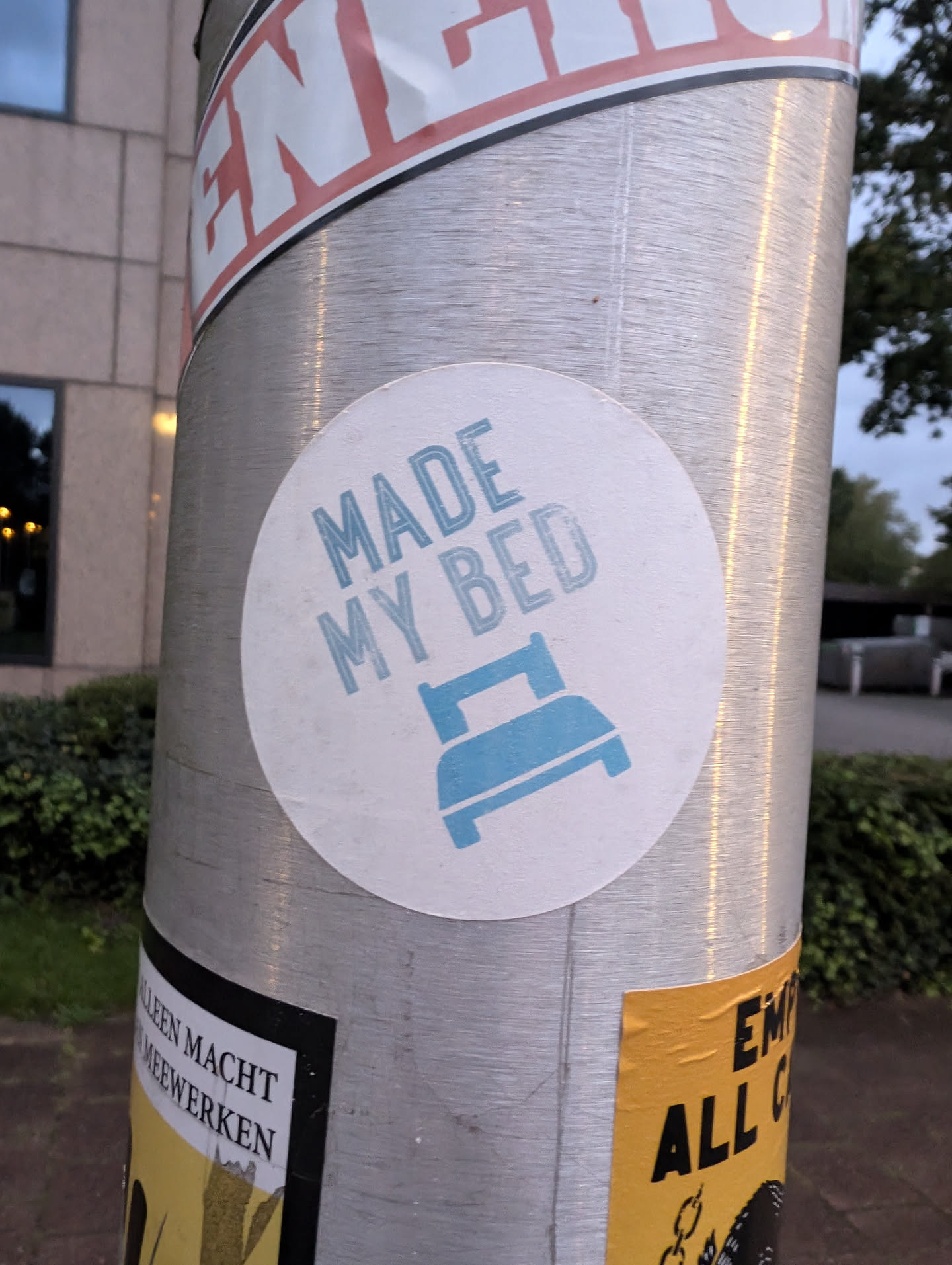 A round sticker with the text 'Made my bed' and an icon of a bed. The sticker is on a metal pole.