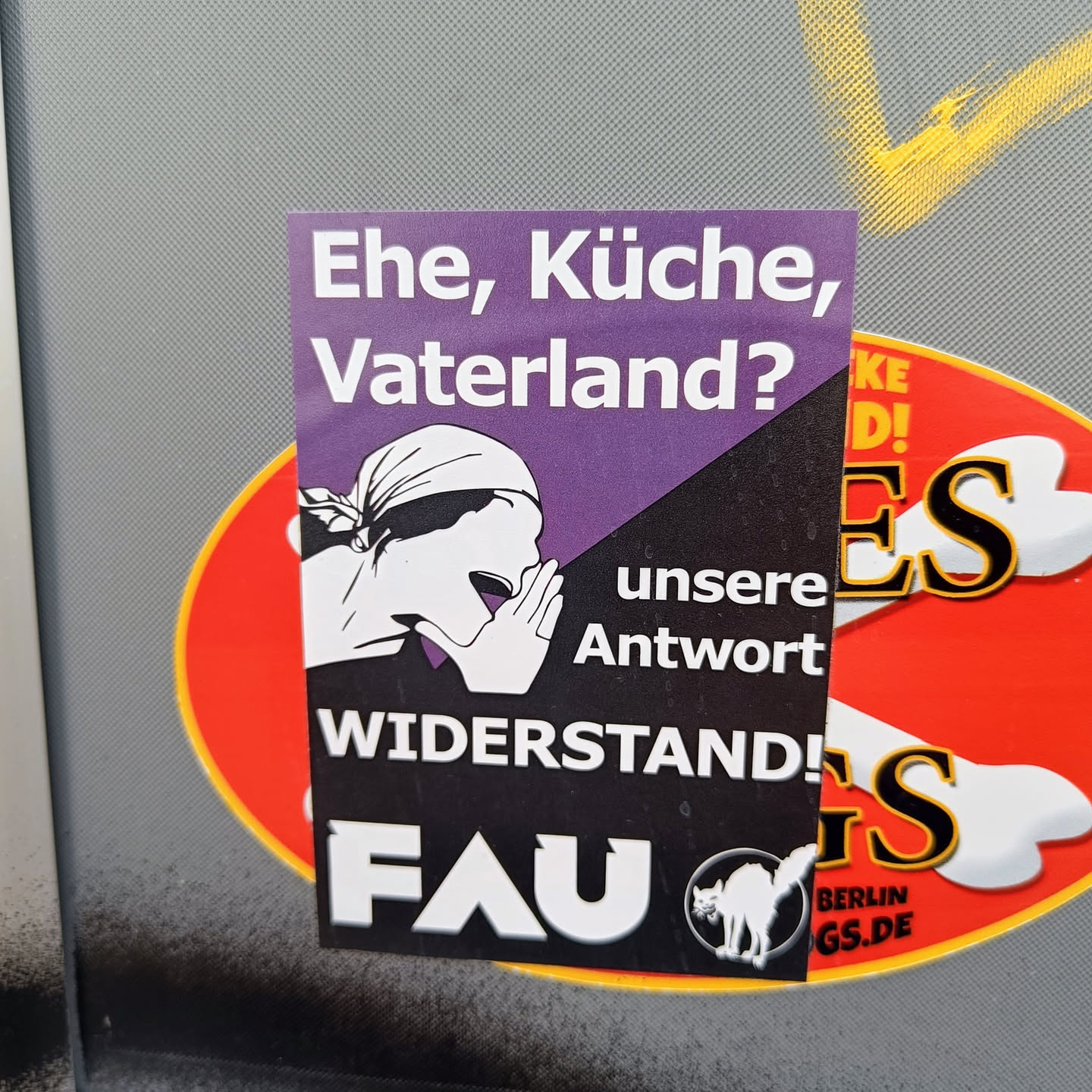 A sticker featuring a black and purple design with a stylized image of a person shouting.  The text includes the German phrases "Ehe, Küche, Vaterland?" (Wife, Kitchen, Fatherland?), "unsere Antwort" (our answer), and "WIDERSTAND!" (Resistance!).  The acronym FAU is prominently displayed, along with a black cat illustration.  The sticker conveys a message of resistance against traditional gender roles.