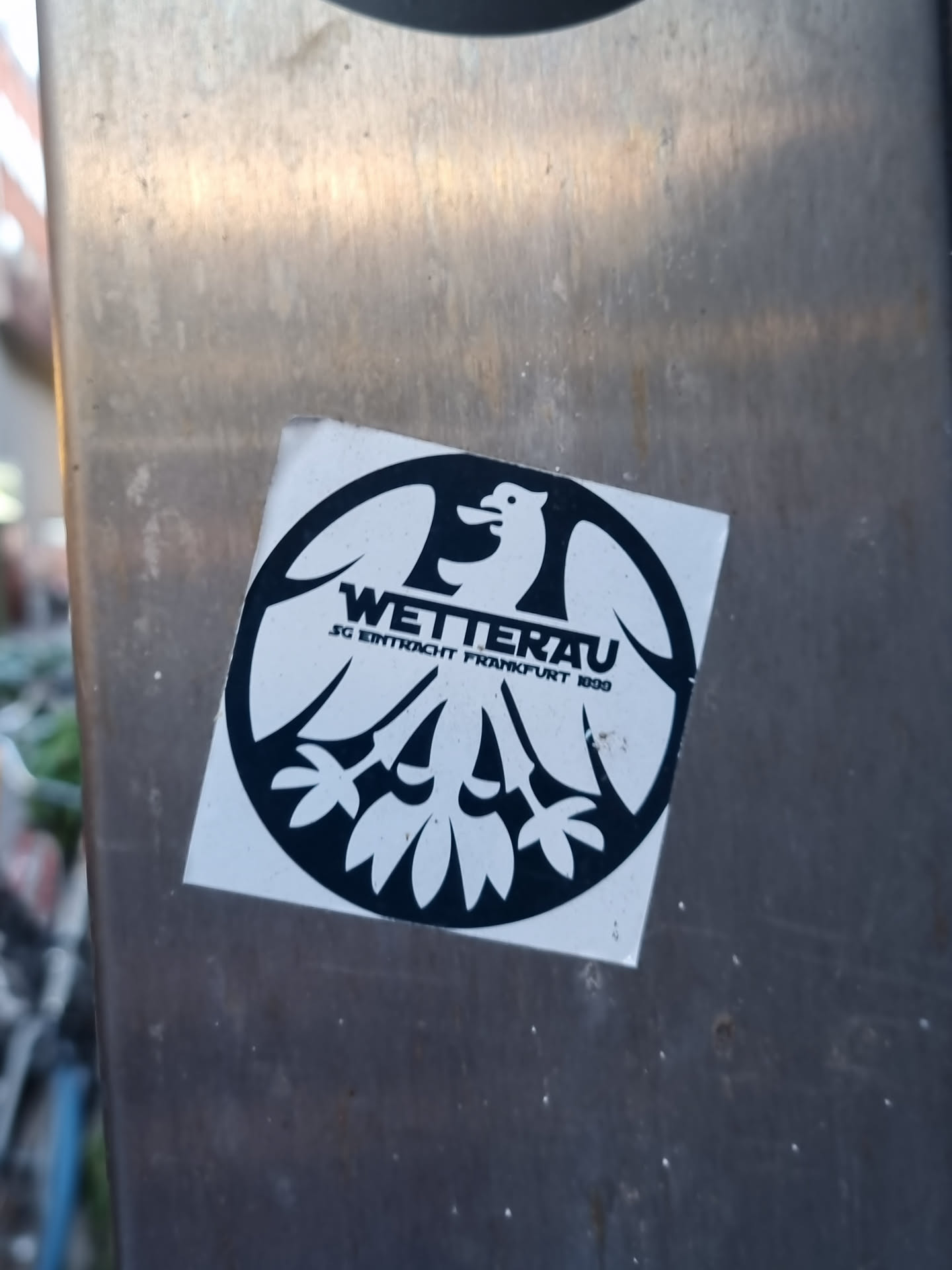 Black and white circular sticker featuring a stylized bird emblem with text. The text includes 'WETTERAU' and 'SG EINTRACHT FRANKFURT 1909'.