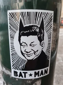 Black and white sticker depicting Xi Jinping with bat ears, in the style of propaganda art. Text at the bottom reads "BAT☆MAN".
