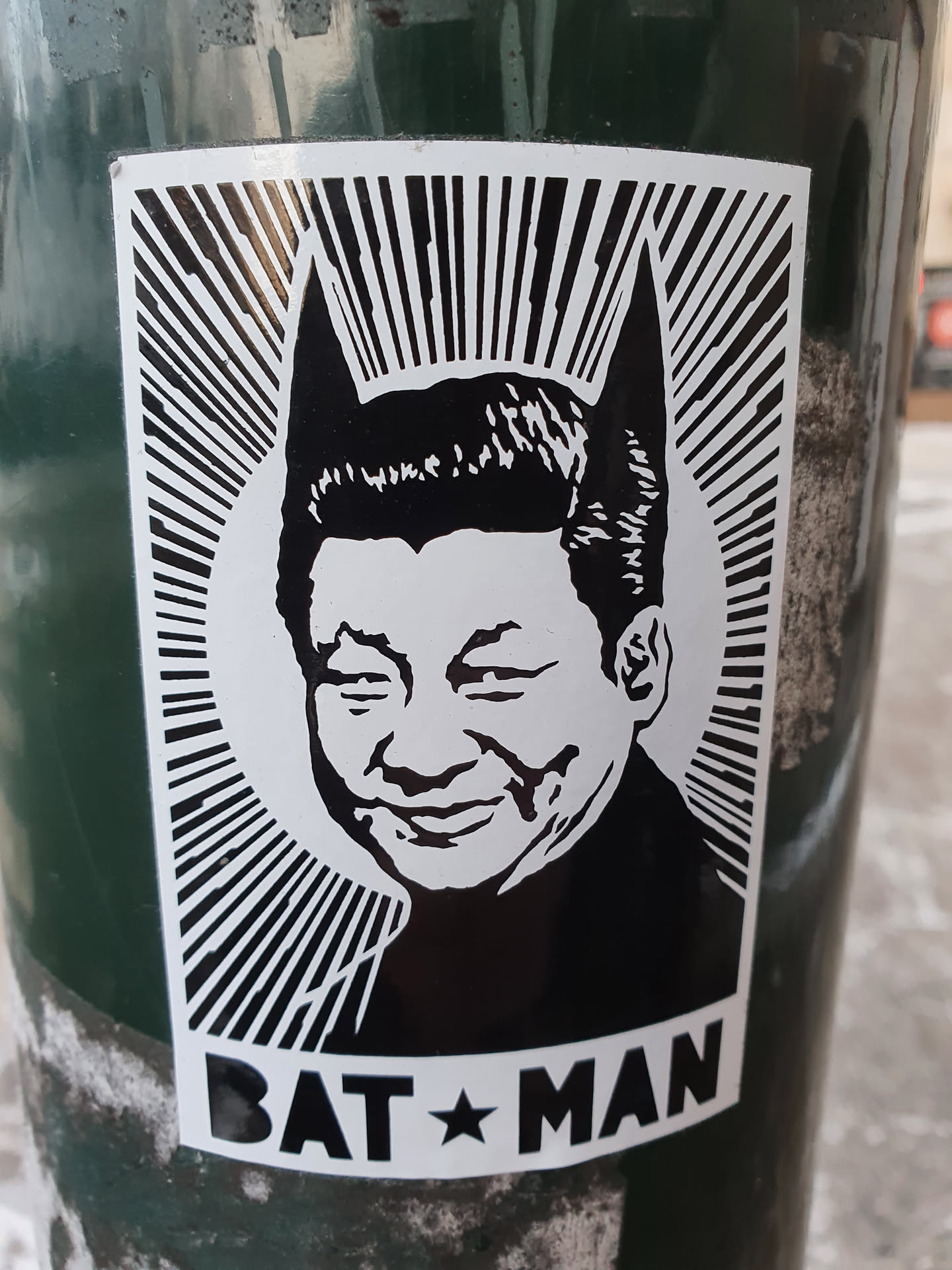 Black and white sticker depicting Xi Jinping with bat ears, in the style of propaganda art. Text at the bottom reads "BAT☆MAN".