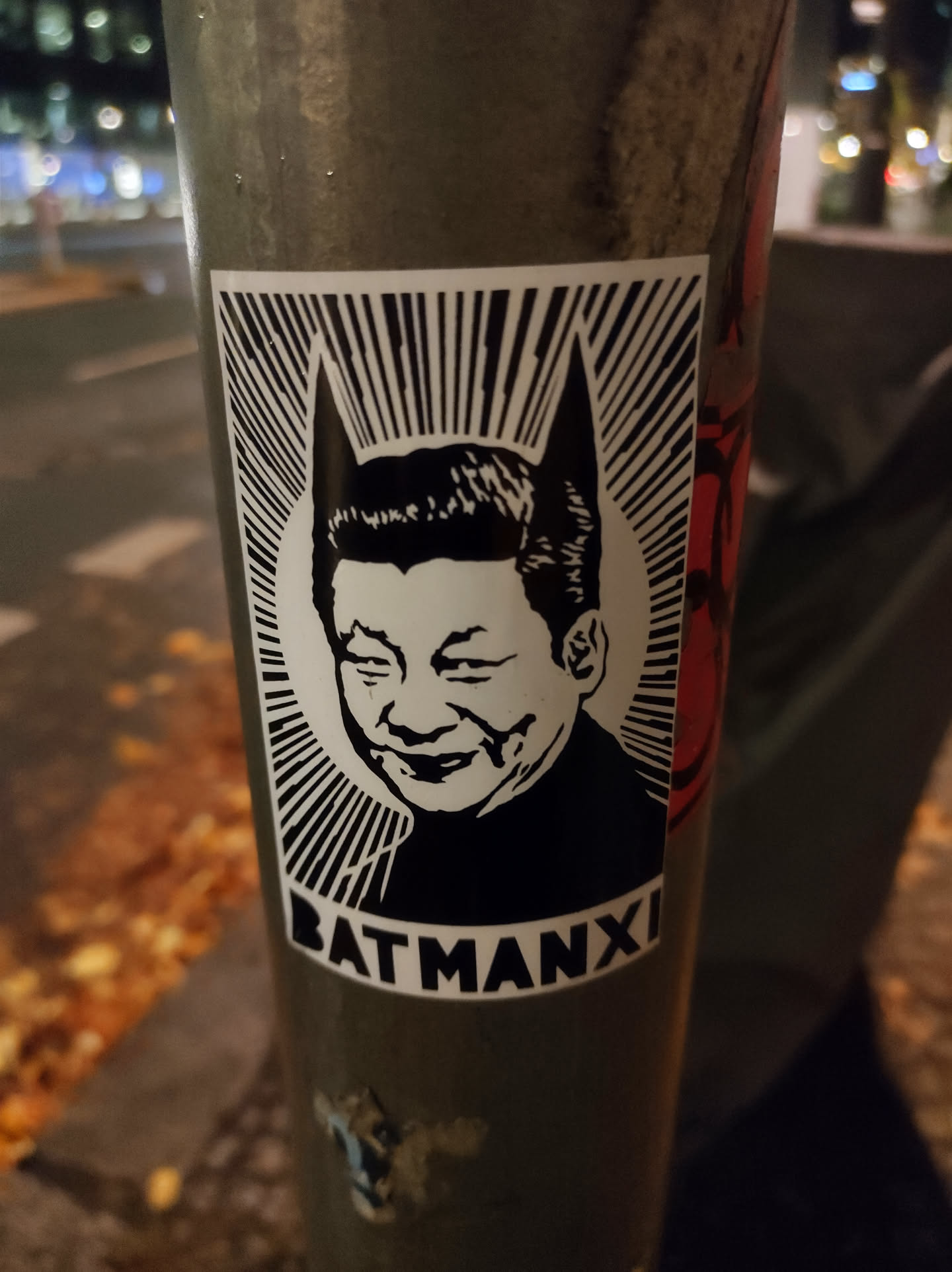 A sticker featuring a stylized image of Xi Jinping with bat ears, resembling Batman. The sticker is in black and white with the text "BATMANXI" at the bottom. 