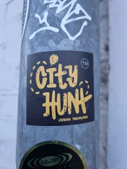 A black sticker with the text City Hunt in yellow.  The words "Urban Treasures" are written in smaller text below the main text. There is a small ™ symbol next to the word Hunt.