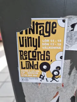 A yellow and black sticker advertising a vintage vinyl record sale in Lund. The sticker features illustrations of two characters carrying vinyl records.  The sale takes place on Saturday (Lör) from 11-15 and Sunday (Sön) from 13-15.