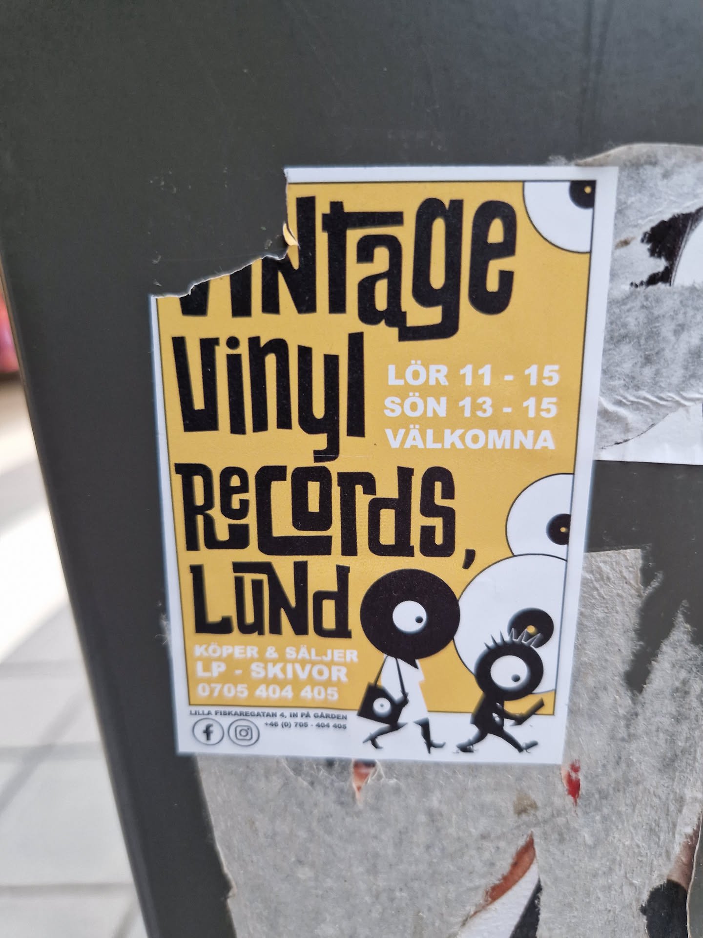 A yellow and black sticker advertising a vintage vinyl record sale in Lund. The sticker features illustrations of two characters carrying vinyl records.  The sale takes place on Saturday (Lör) from 11-15 and Sunday (Sön) from 13-15.