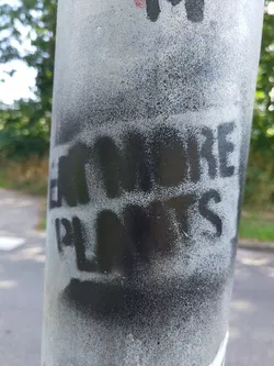 A black and white stencil graffiti on a grey pole. The text is slightly faded and worn.