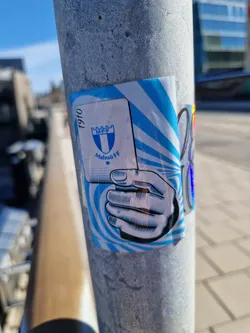 A sticker featuring the Malmö FF logo, a hand holding a playing card, and the year 1910. The design incorporates blue and white colors and a swirling pattern.
