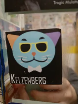 A sticker featuring a cartoon cat wearing sunglasses and a bow tie. The cat's ears are different colors. The text "Kelzenberg" is at the bottom of the sticker.